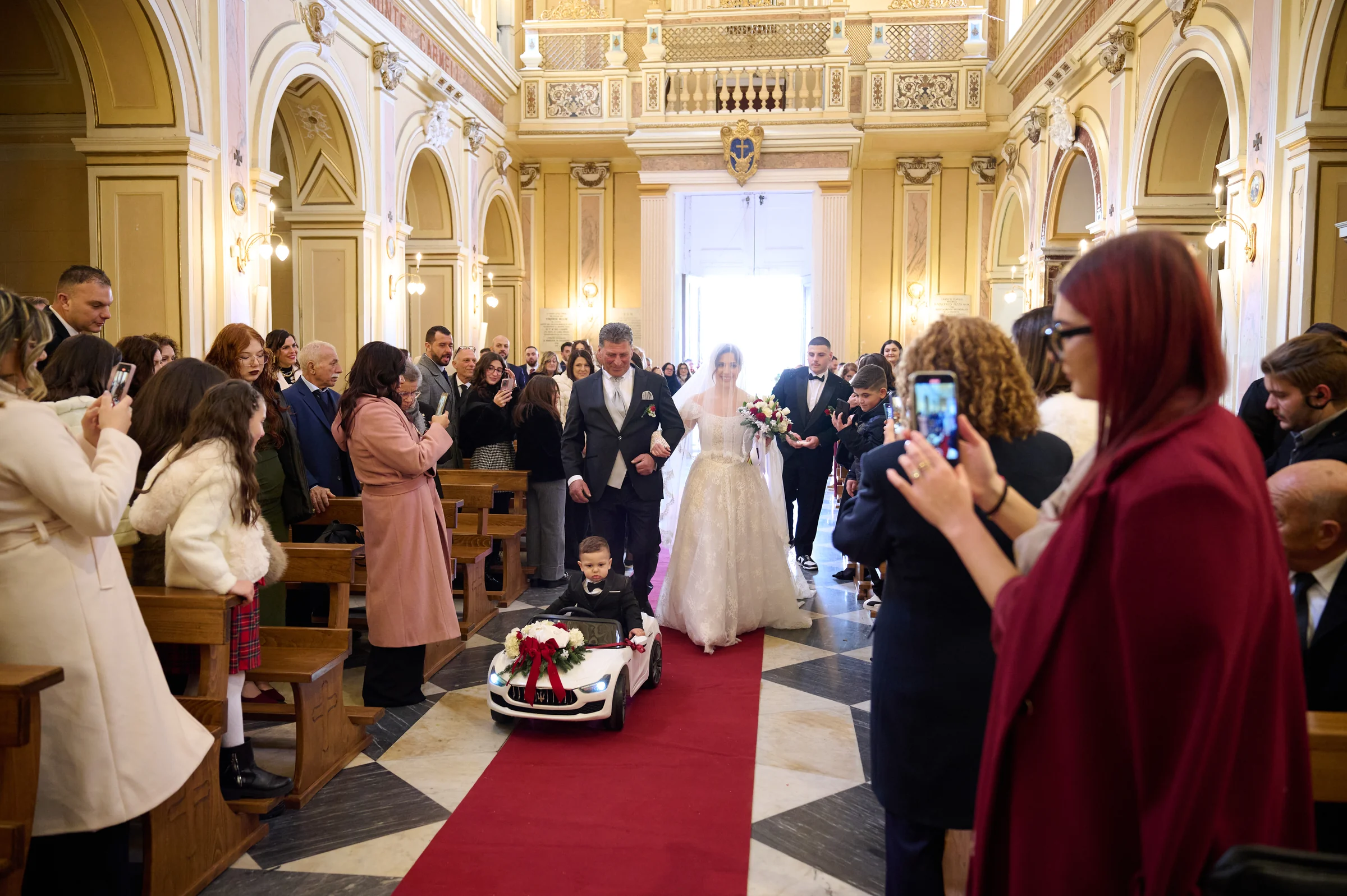 Rosa entering the sanctuary in Gragnano, with guests lining the aisle and a child in a small car ahead.