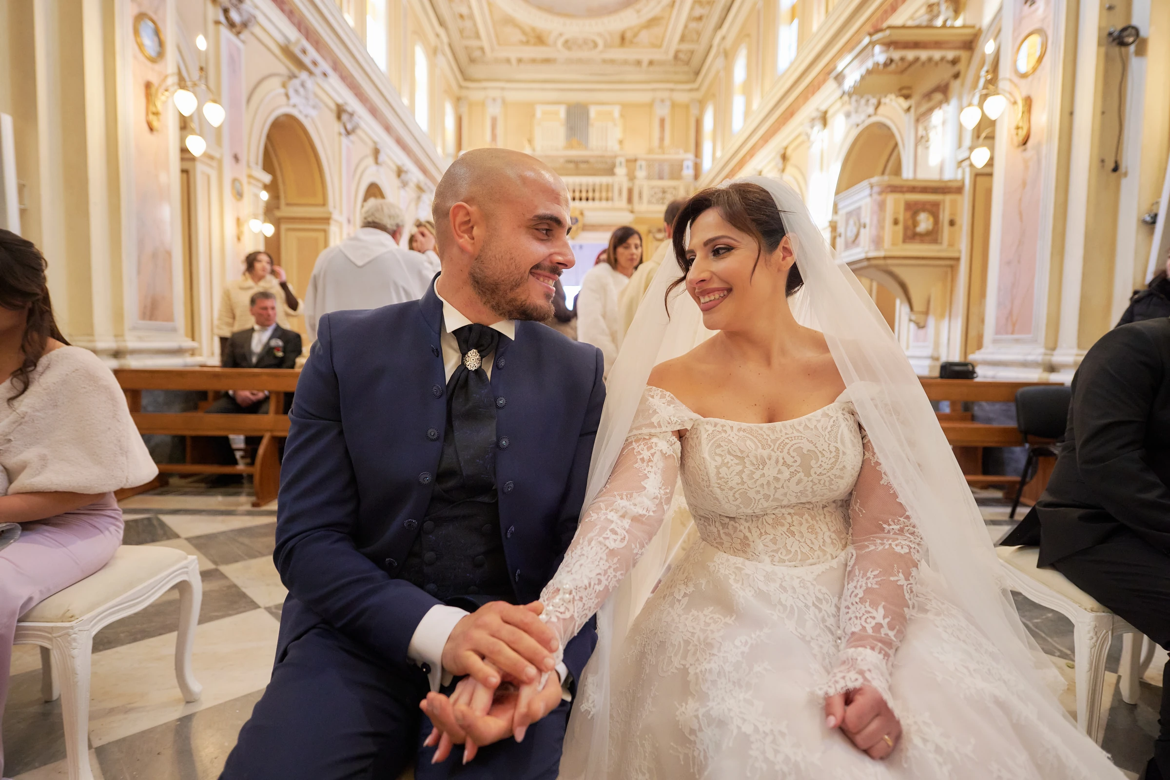 Ciro and Rosa smiling at each other and holding hands while seated in the sanctuary in Gragnano.