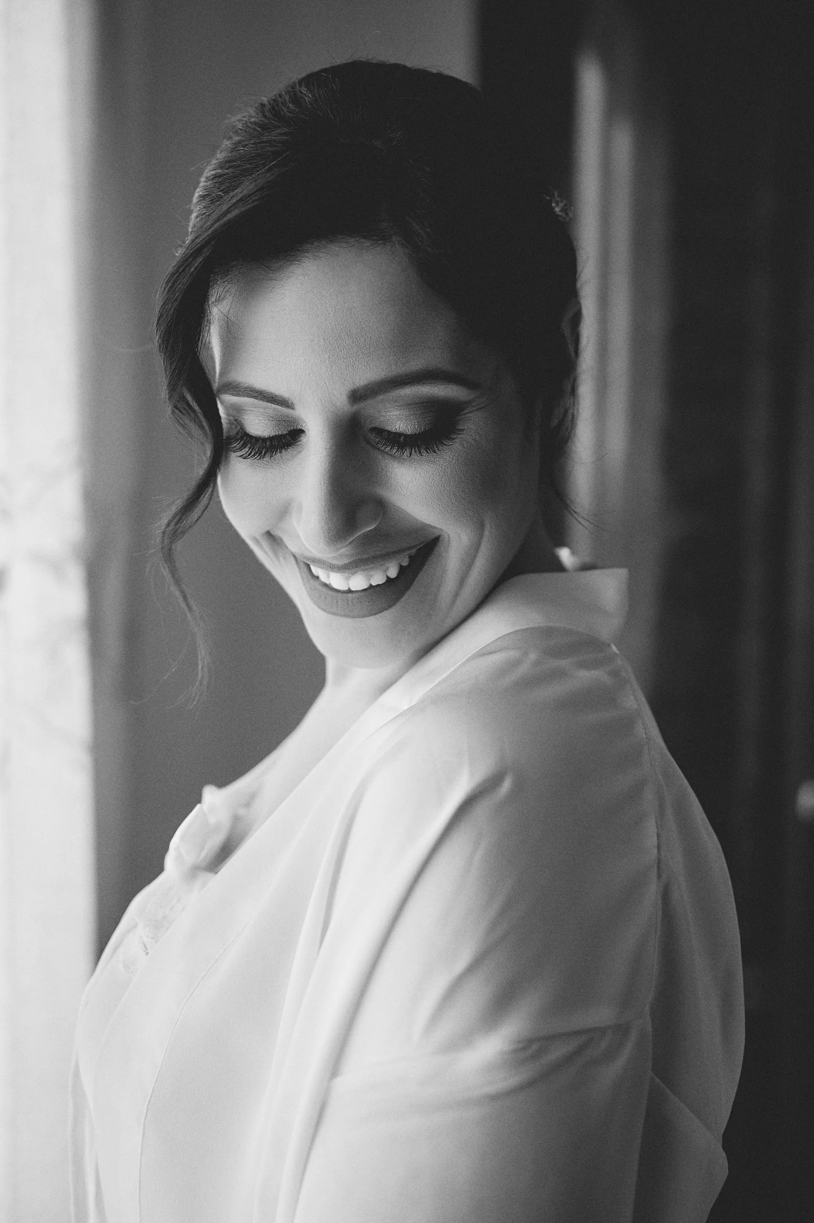 Black and white portrait of Rosa smiling beside a window in her bridal robe.
