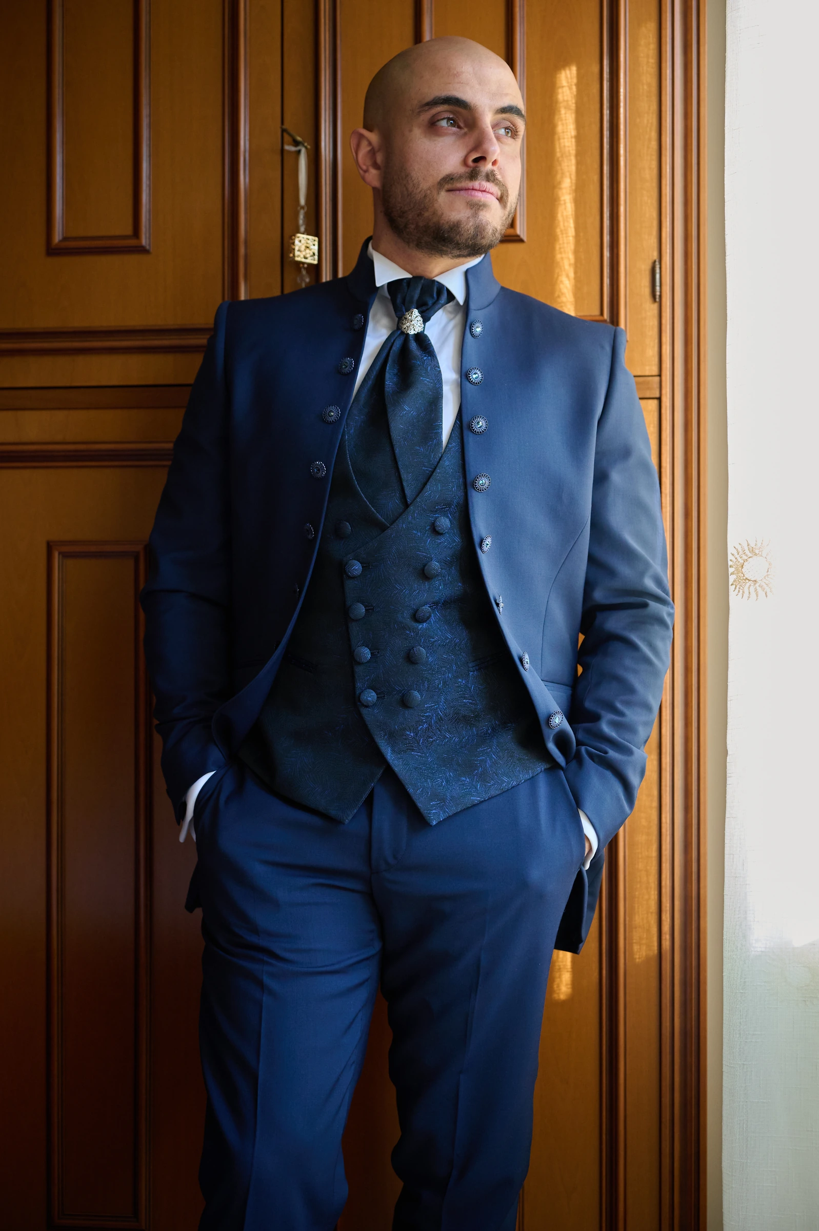 Ciro standing beside a window in his blue wedding suit.