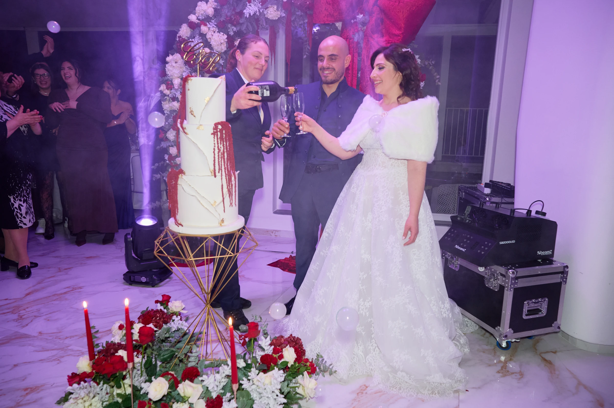 Ciro and Rosa raising their glasses beside the wedding cake under purple reception lighting at Le Rocce in Agerola.
