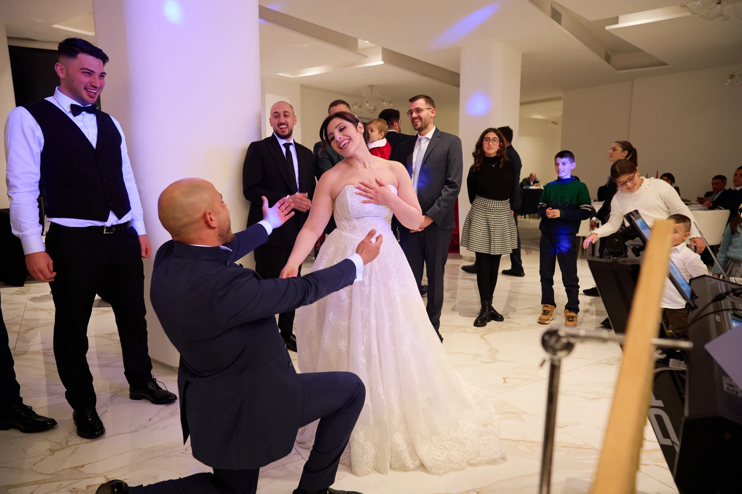 Ciro kneeling in front of a laughing Rosa during a playful moment at their wedding reception at Le Rocce in Agerola.