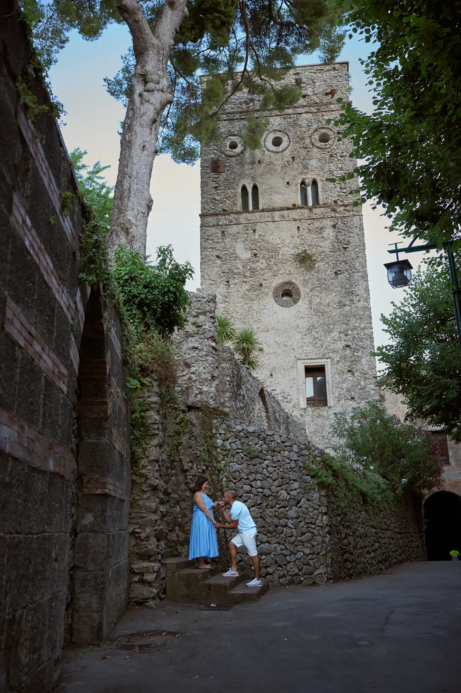 Ciro and Rosa standing together beneath a stone tower during their engagement walk in Ravello.