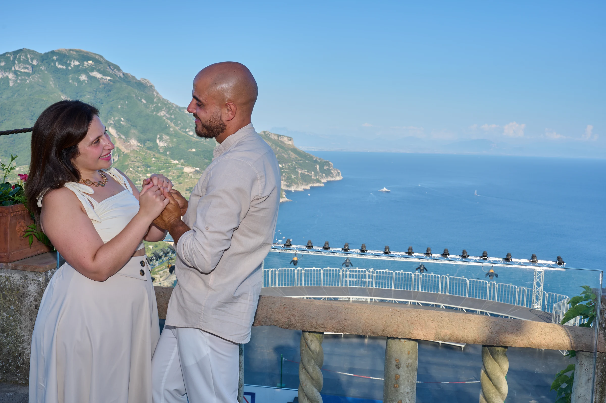 Ciro and Rosa embracing on a terrace at Villa Rufolo, with the Amalfi Coast and sea in the background.