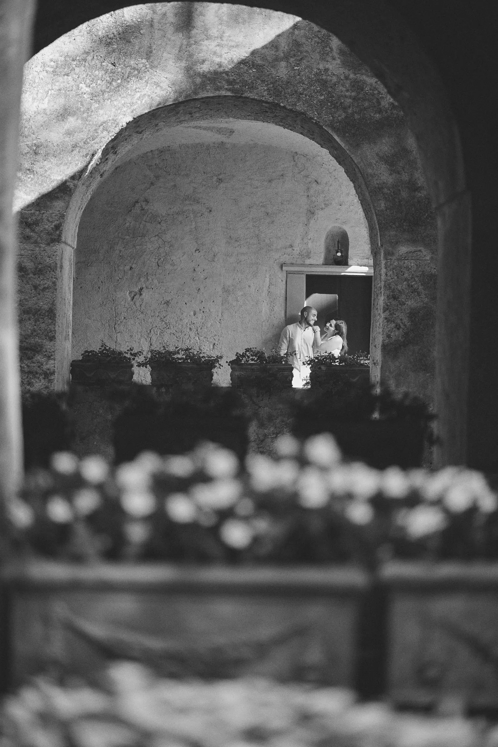 Ciro and Rosa framed by a stone arch and foreground flowers at Villa Rufolo in Ravello.