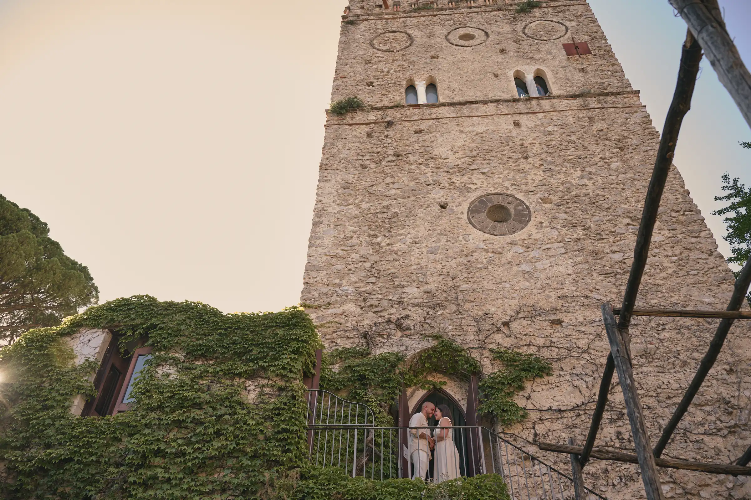 Ciro and Rosa beneath the stone tower at Villa Rufolo, surrounded by greenery in Ravello.