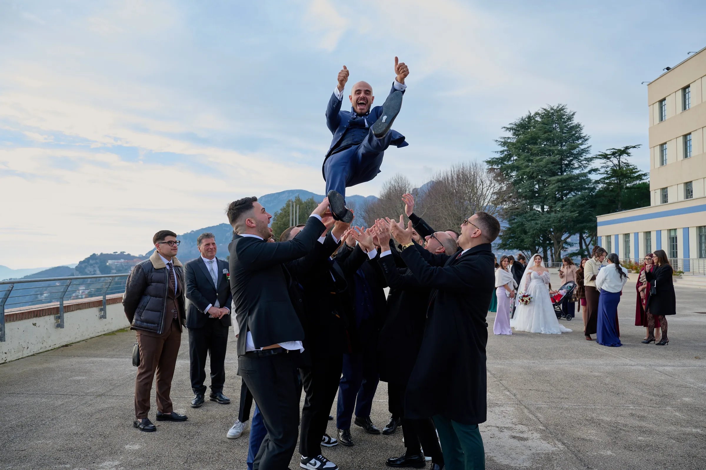 Ciro being lifted into the air by a group of wedding guests as Rosa watches nearby.