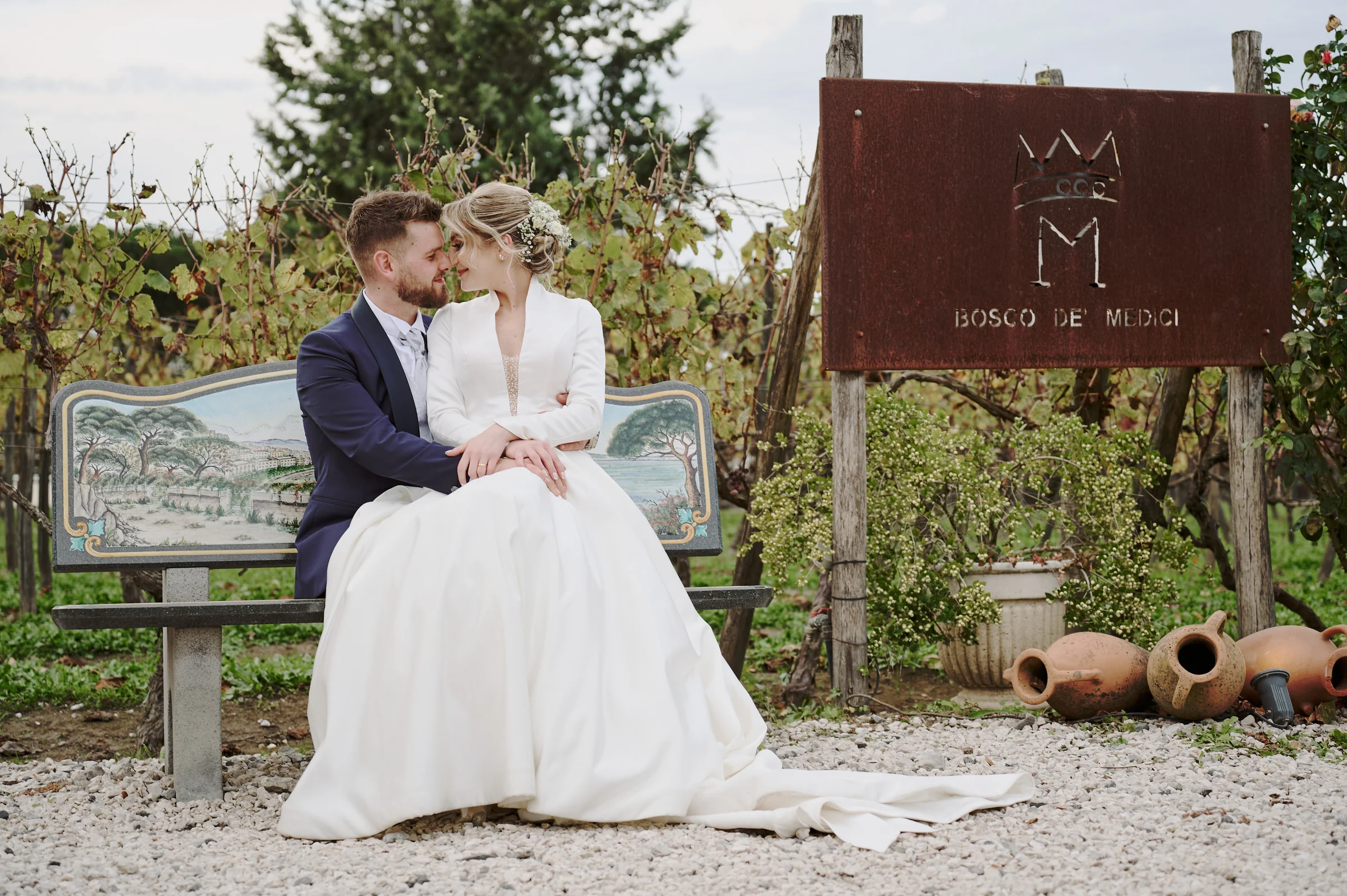 Matteo and Clementina seated on a bench beside the Bosco de’ Medici sign in Pompei.
