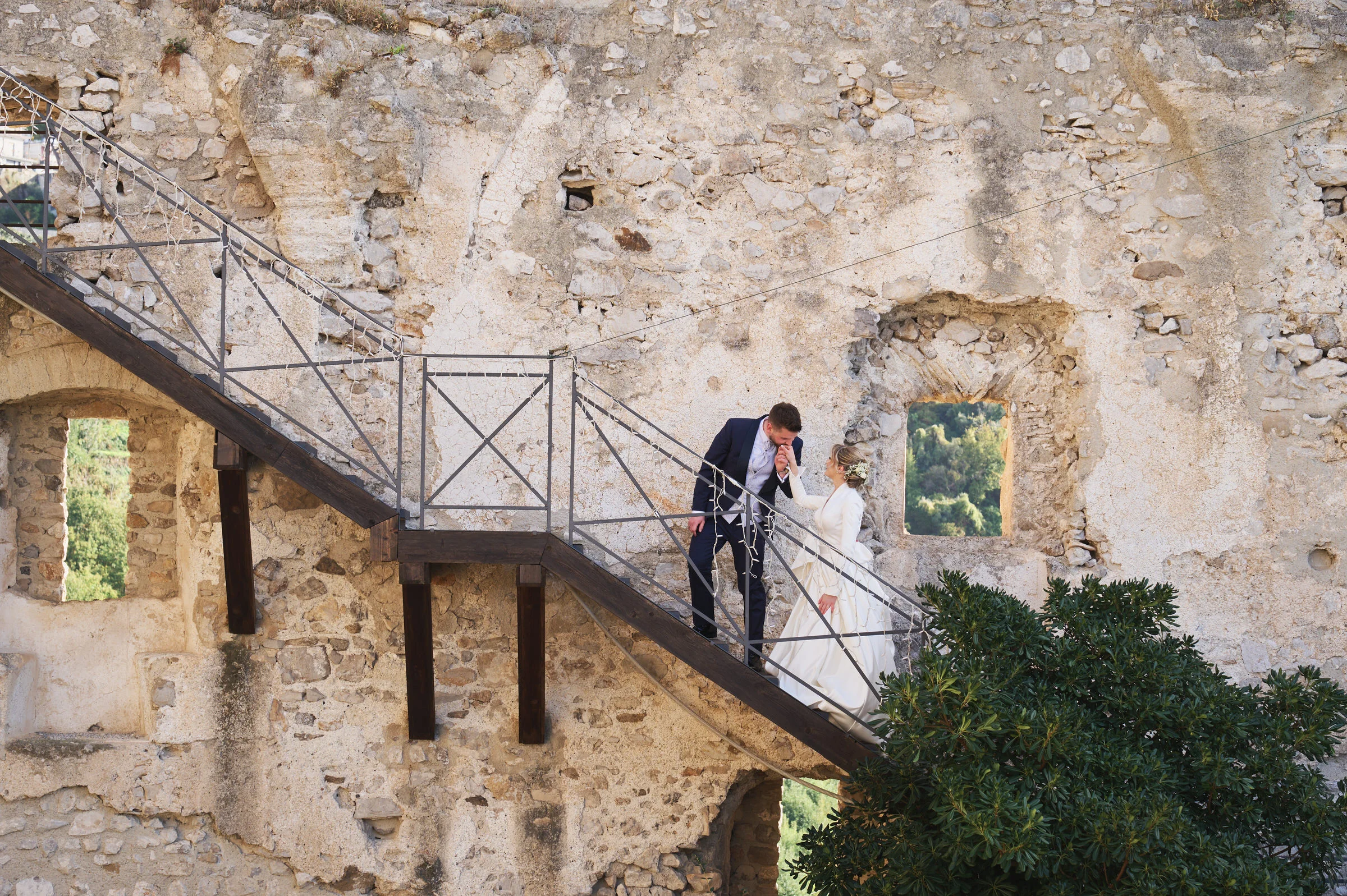 Matteo kissing Clementina’s hand on a staircase against stone walls in Lettere Castle