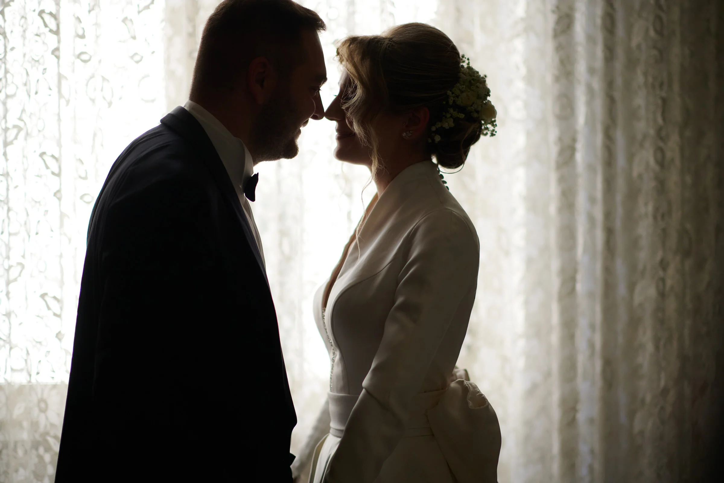 Clementina and her brother leaning towards each other, backlit by a window during her wedding preparations in Gragnano.